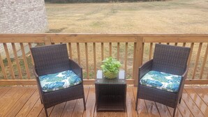 A wooden deck with two wicker chairs and a small table, each with a plant on it. - Cozy 3-bedroom house in charming small town Sedley (Sedley)