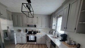 A modern kitchen with white cabinetry, a stainless steel refrigerator, a microwave, and a stove. - Cozy 3-bedroom house in charming small town Sedley (Sedley)