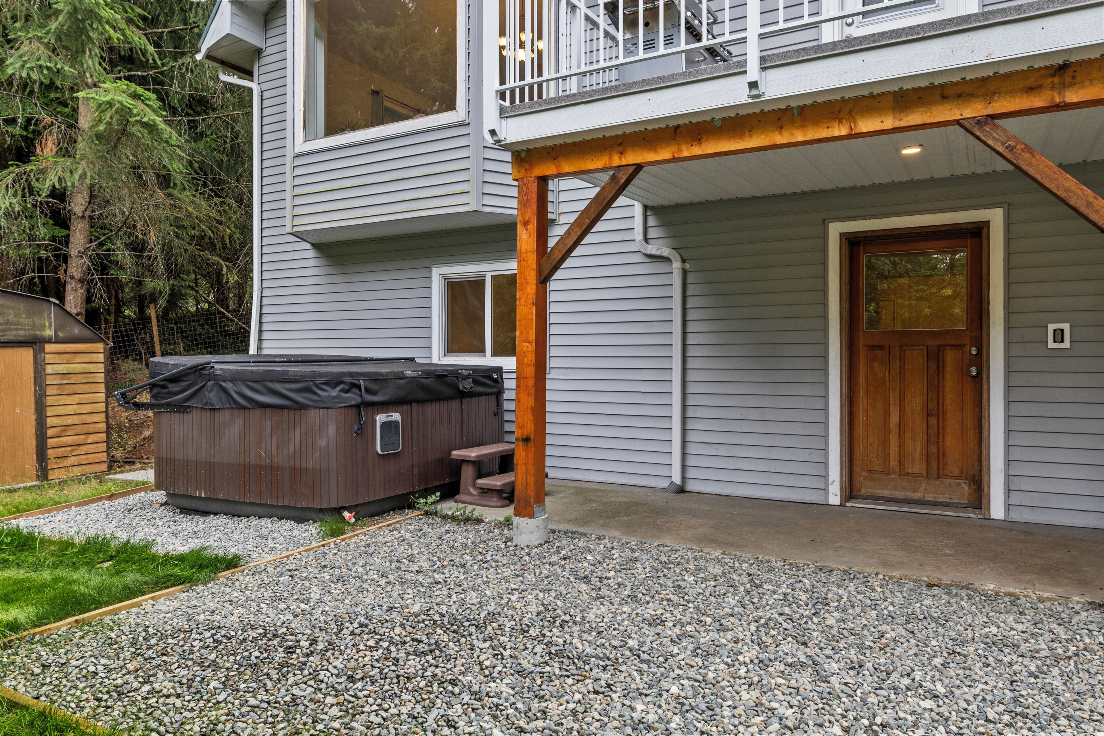 A two-story house with a covered hot tub, a wooden deck, and a gravel driveway.