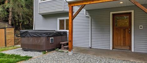 A two-story house with a covered hot tub, a wooden deck, and a gravel driveway.