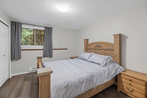 Une chambre à coucher avec un lit en bois, une table de chevet, une commode et une fenêtre avec des rideaux.