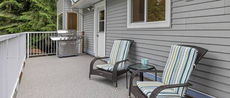 A covered outdoor area with wicker chairs, a table, and a grill.