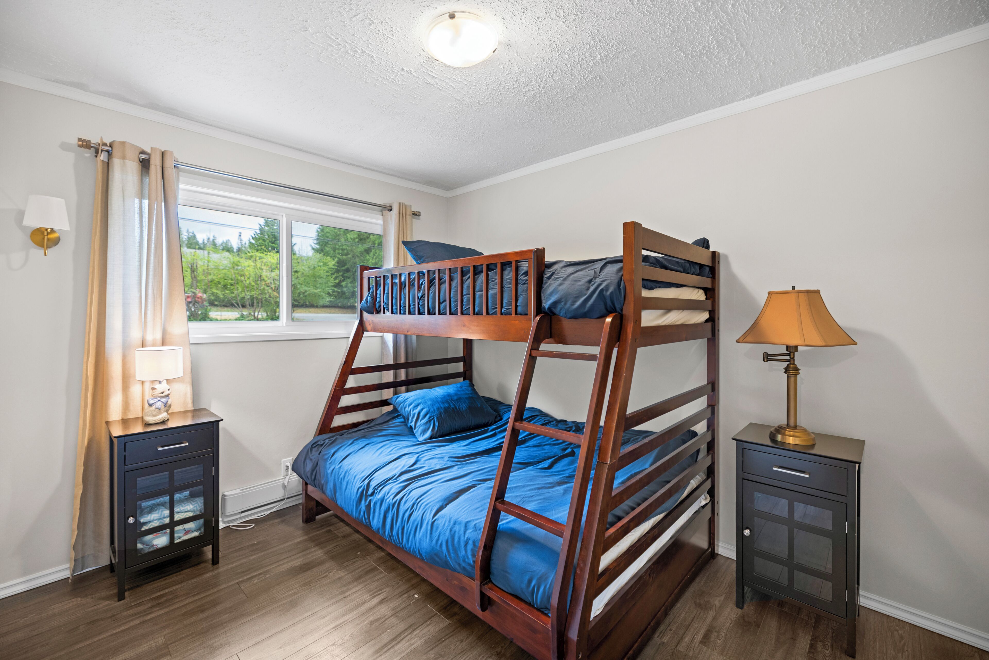 A bunk bed room with a window, bedside tables, and a lamp.