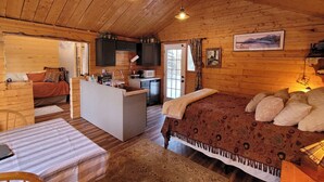 A cozy cabin interior with a wooden ceiling, a bed with patterned bedding, a dining area, and a kitchen with dark cabinets. - The Polaris is a cozy delight with 360 degree mountain views.  Pet Friendly! (Sutton)