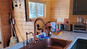 A wooden cabin kitchen with a copper sink, wooden cabinets, and a window overlooking a snowy landscape. - The Polaris is a cozy delight with 360 degree mountain views.  Pet Friendly! (Sutton)