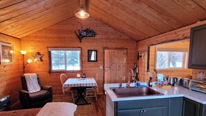 A cozy cabin interior with a dining area, kitchen, and a large window providing natural light. - The Polaris is a cozy delight with 360 degree mountain views.  Pet Friendly! (Sutton)