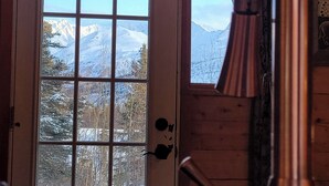 A wooden cabin interior with a large window overlooking a snowy mountain landscape. - The Polaris is a cozy delight with 360 degree mountain views.  Pet Friendly! (Sutton)