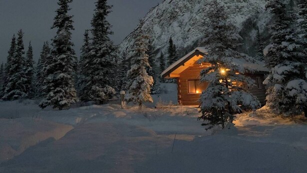 A cabin in a snowy mountainous area at night with a visible moon.