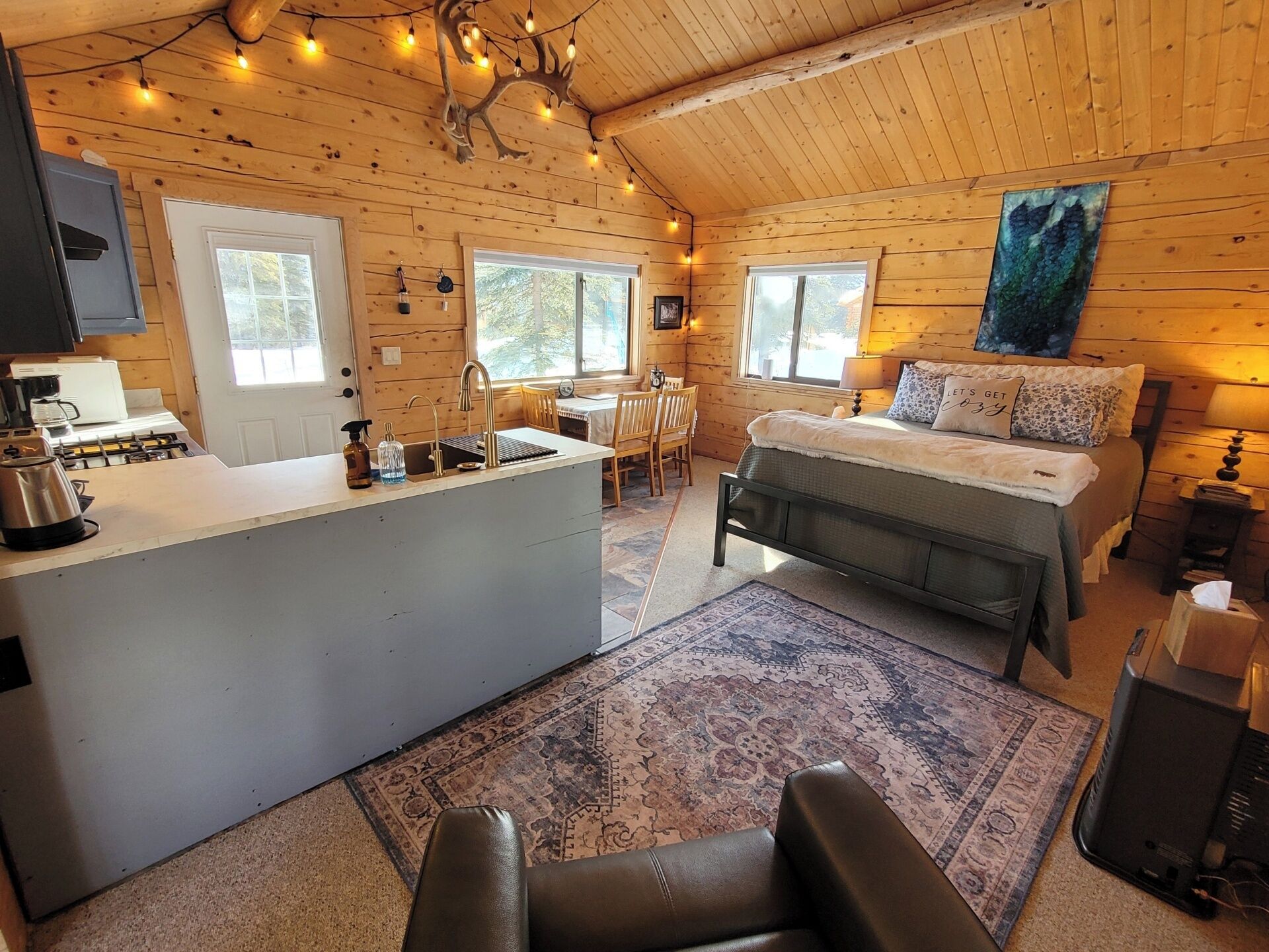 A cozy cabin interior with a kitchen, dining area, and a bed.