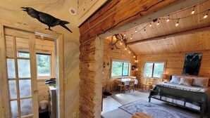 A cozy cabin with a wooden interior, a dining area, a bed, and a ceiling-mounted bird.