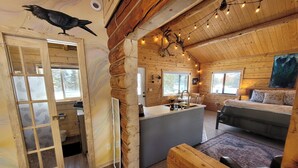 A log cabin interior with a kitchen, dining area, and a bed with a 'Let's Get Cozy' pillow.