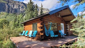 A log cabin with a deck, blue chairs, and a hammock.
