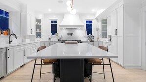 A modern kitchen with white cabinetry, a large island, and pendant lighting. - SOWDEN HOUSE - Amazing & unique home located less than 20 minutes to down town. (North Vancouver)