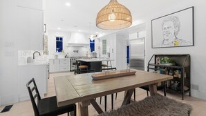 A modern kitchen with white cabinetry, a central island, and a dining area with a wooden table and chairs. - SOWDEN HOUSE - Amazing & unique home located less than 20 minutes to down town. (North Vancouver)