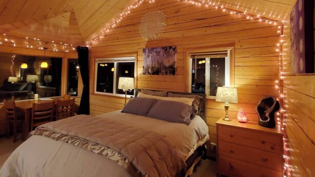 Een gezellig houten slaapkamer met een bed, twee nachtkastjes, een bureau met stoelen en lichtjes.