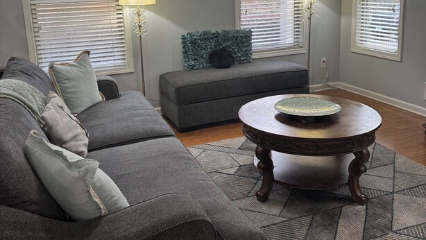 Ein Wohnzimmer mit einem grauen Ecksofa, einem runden Couchtisch und einem grauen Teppich.
