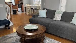 Ein Wohnzimmer mit einem grauen Sofa, einem Holztisch und einem gemusterten Teppich.