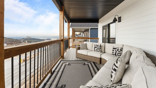 Een balkon met een bank, een kleed met een patroon en uitzicht op een gebouw in de verte.