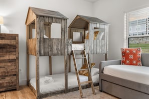 A room with two wooden bunk beds, a grey sofa, a wooden dresser, and a window with a view of a building. - Stunning Lakeview,HotTub,Game Room,Pools,Sleeps 16 (Branson)
