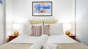 Ein ordentlich bezogenes Bett mit weißen Leinen, zwei Nachttische mit Lampen und ein gerahmtes Kunstwerk von Claude Monets ‚Impression, Sonnenaufgang‘ an der Wand.