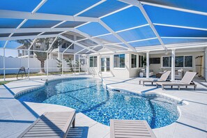 A swimming pool with a covered area, lounge chairs, and a palm tree. - Red Key Beach in Redington Beach – 3BR Retreat with Screened-In Heated Pool Oasis (Redington Beach)