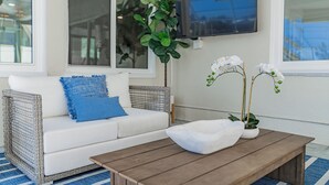 Un saló amb un sofà blanc, un coixí blau, una taula de centre de fusta, plantes d'orquídea blanca i un televisor fixat a la paret.