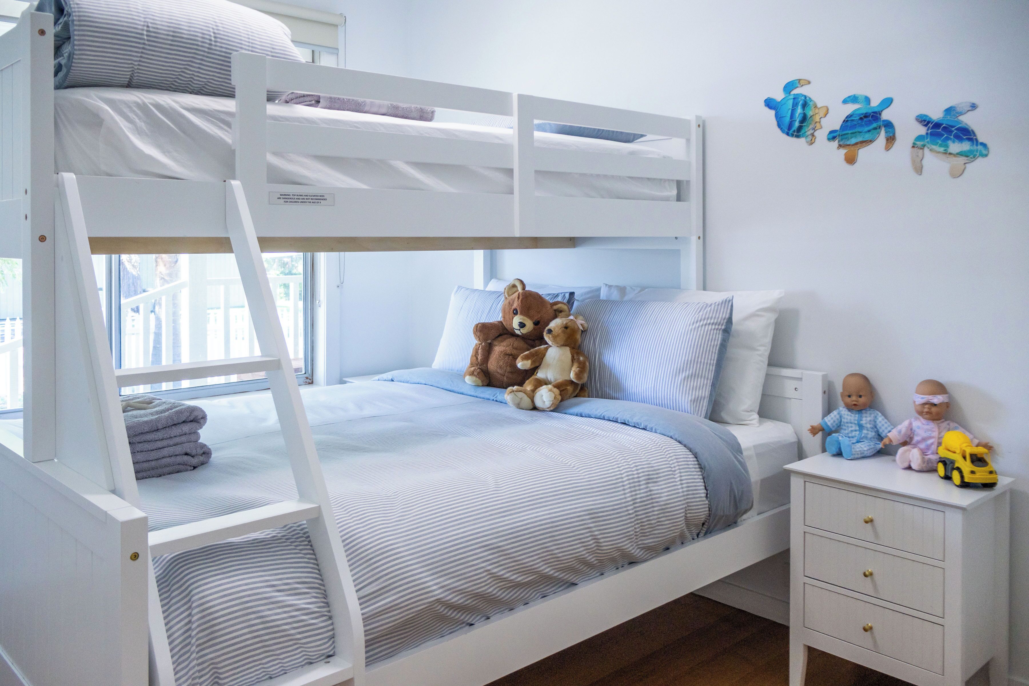 A bunk bed room with a white dresser, a nightstand, and a wall decoration of sea turtles.