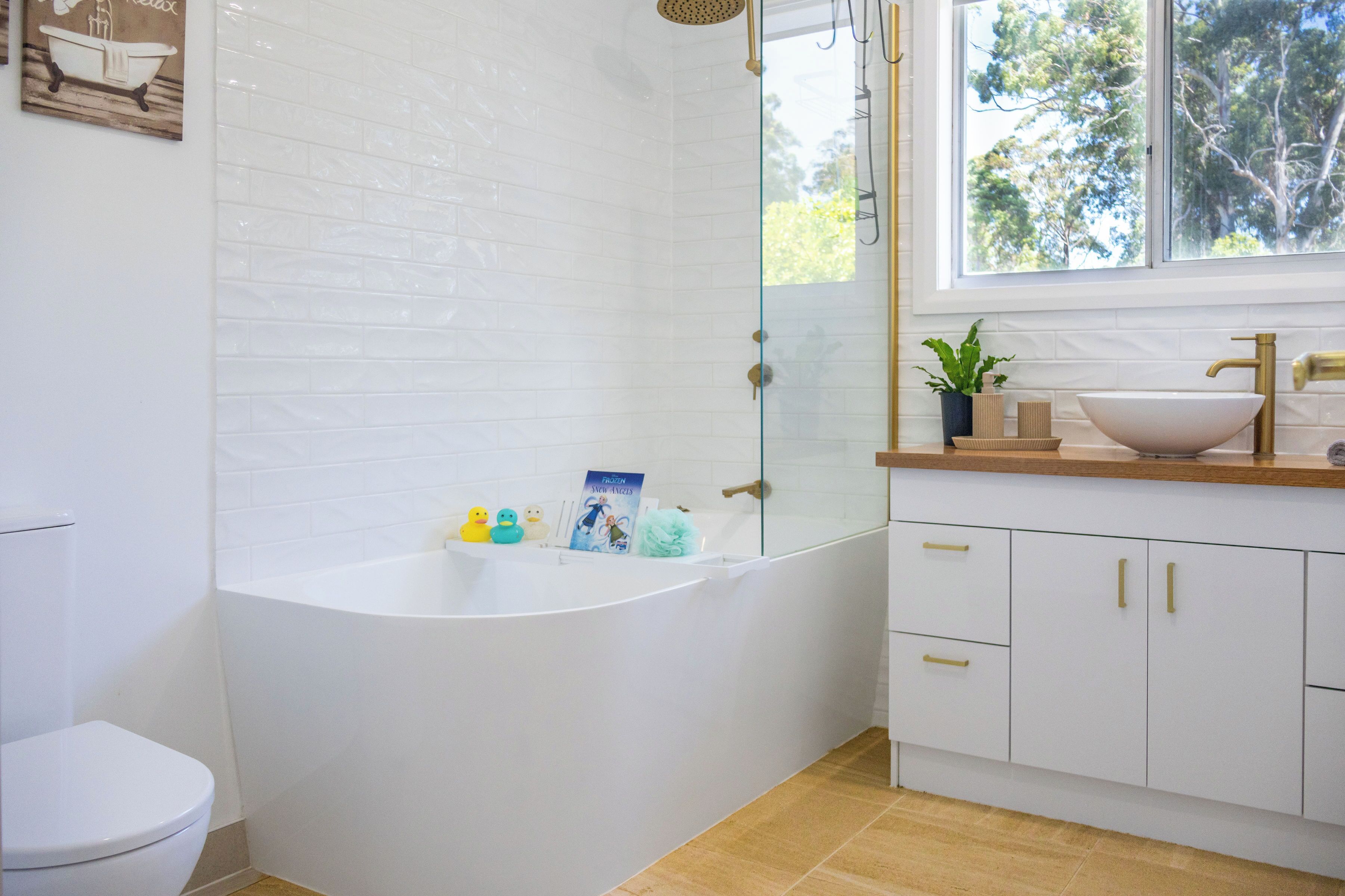 A modern bathroom with a freestanding bathtub, a white toilet, and a window with a view of trees.