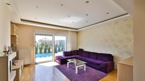 A modern living room with a purple sectional sofa, a glass coffee table, and a view of a swimming pool through a sliding glass door. - Awesome home in Kastel Luksic (Kastel Luksic)