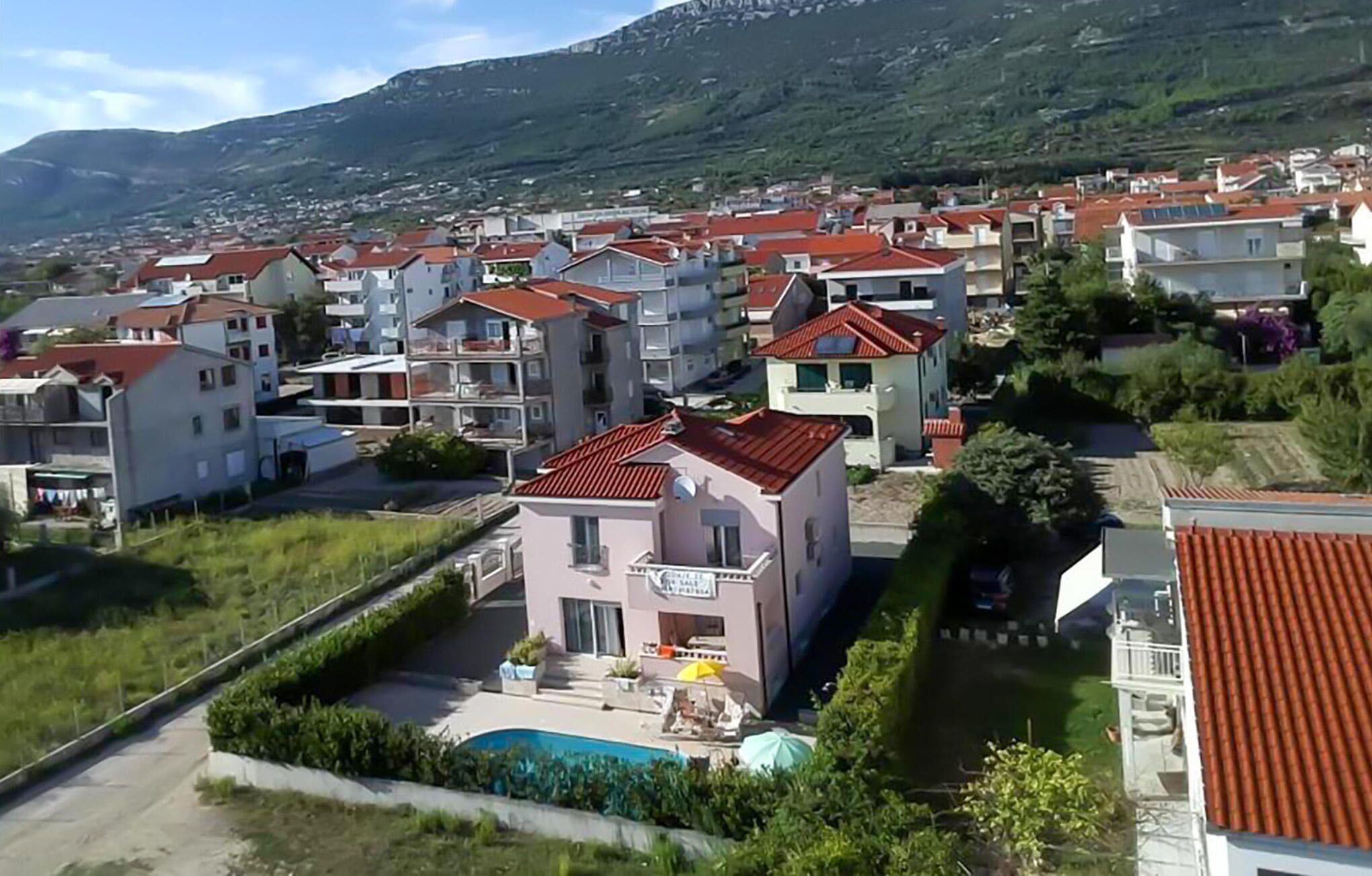 A residential area with multiple two-story houses, a swimming pool, and a mountainous backdrop.