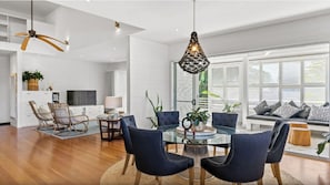 Ein modernes Wohnzimmer mit einem Glastisch, dunkelblauen Polsterstühlen, einem Deckenventilator und einer einzigartigen gewebten Lampe.