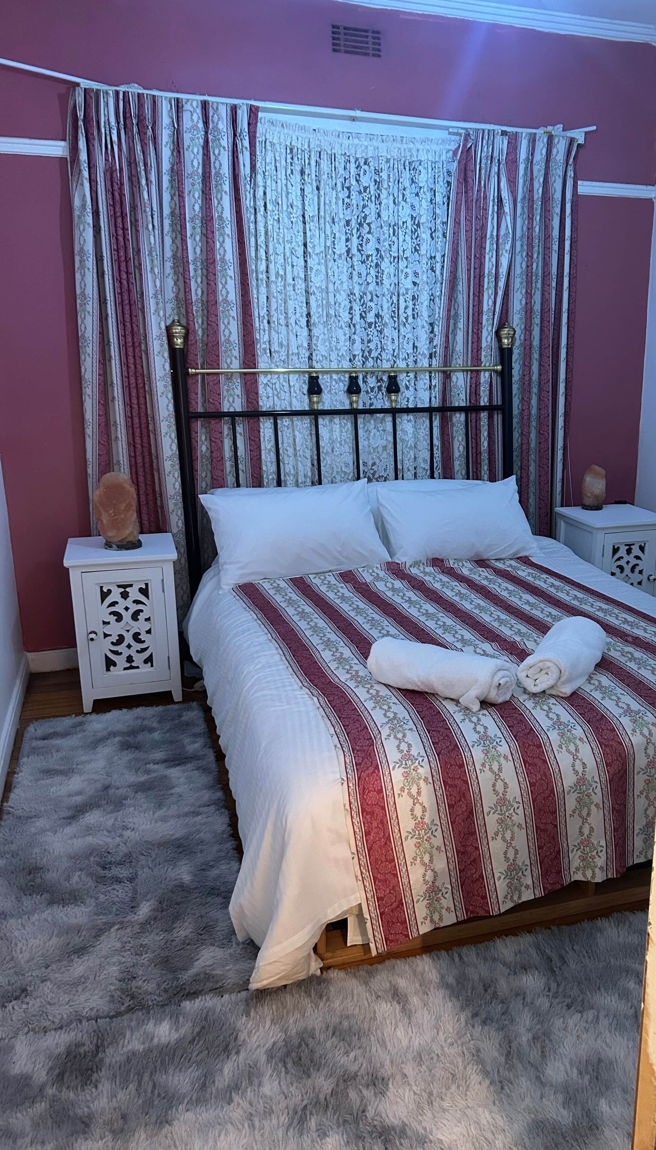 Een slaapkamer met een bed, twee nachtkastjes, een zacht tapijt en een raam met gordijnen.