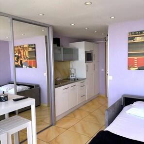 A compact hotel room with a kitchenette, a bed, a small table, and a mirror. - IRIS - Studio Héliopolis C13 - Luxury - 2 people (AGDE)