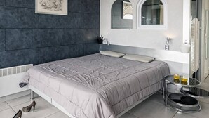 A modern bedroom with a large bed, a dark accent wall, a framed artwork, a bedside table with a lamp, and a small round mirror. - LANA - Studio Héliopolis C14 - Luxury - 2 people (AGDE)