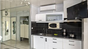 A modern kitchen with white cabinets, a microwave, a stove, and a flat-screen TV. - LANA - Studio Héliopolis C14 - Luxury - 2 people (AGDE)