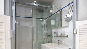 A modern bathroom with a glass-enclosed shower, a white vanity with a mirror, and a small shelf with toiletries. - LANA - Studio Héliopolis C14 - Luxury - 2 people (AGDE)