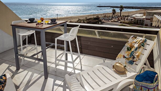 A terrace with a table set for two, white chairs, and a lounge chair with a hat and bag. - LANA - Studio Héliopolis C14 - Luxury - 2 people (AGDE)