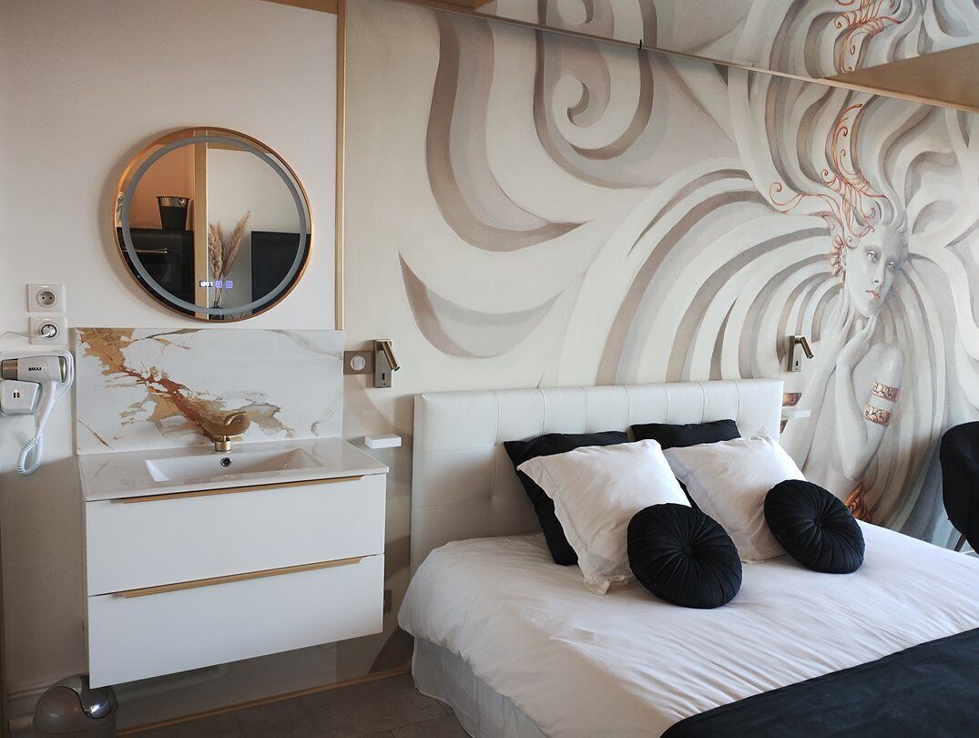A modern bedroom with a white bed, black and white pillows, a round mirror, and a decorative wall with swirling patterns.