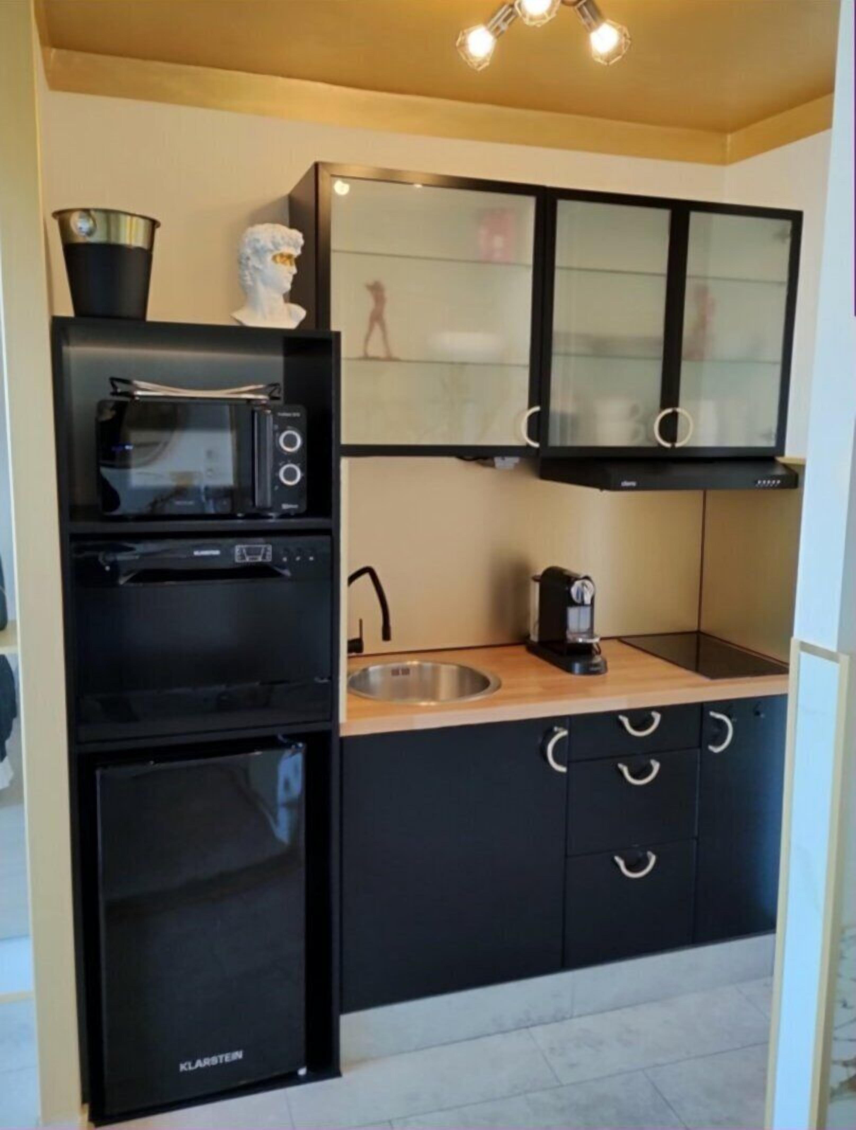 A compact kitchen with black cabinetry, a microwave, a coffee maker, and a small refrigerator.