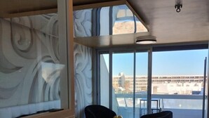 A modern hotel room with a large bed, a small table, a chair, and a view of the city through large windows. - MEDUSE - Studio Héliopolis C29 - Luxury - 2 people (AGDE)