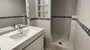 A bathroom with a white sink, a mirror, a shower with a glass door, and decorative tiles. - Studio Héliopolis C 36 - 4 people (AGDE)