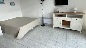 A bedroom with a bed, a TV mounted on the wall, a desk with drawers, and a floor lamp. - Studio Héliopolis C 36 - 4 people (AGDE)