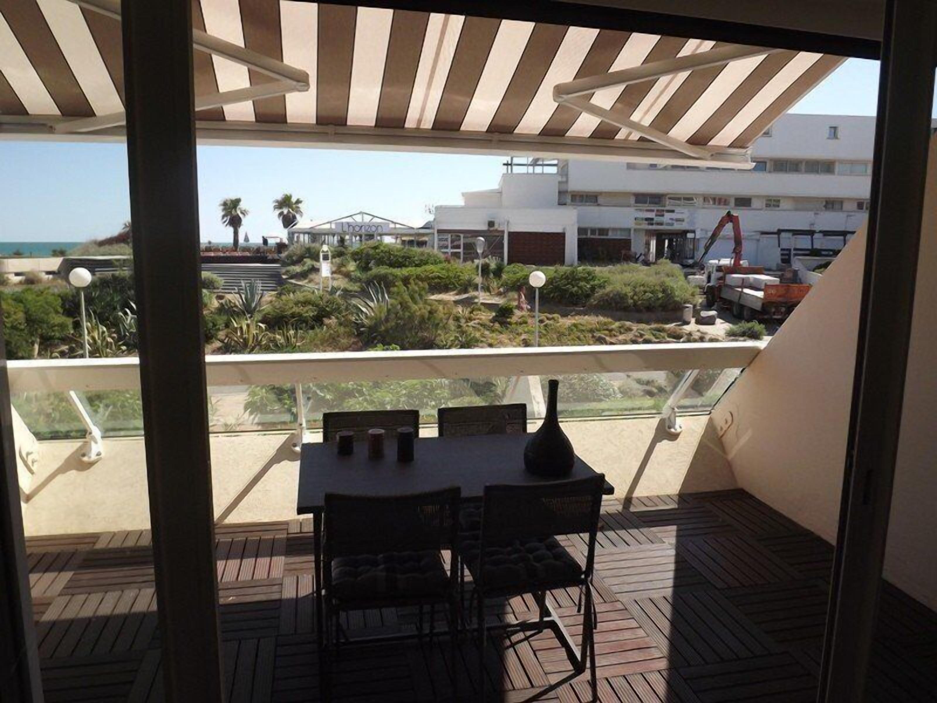 A balcony with a table and chairs, overlooking a landscaped area with a view of buildings and a construction site.