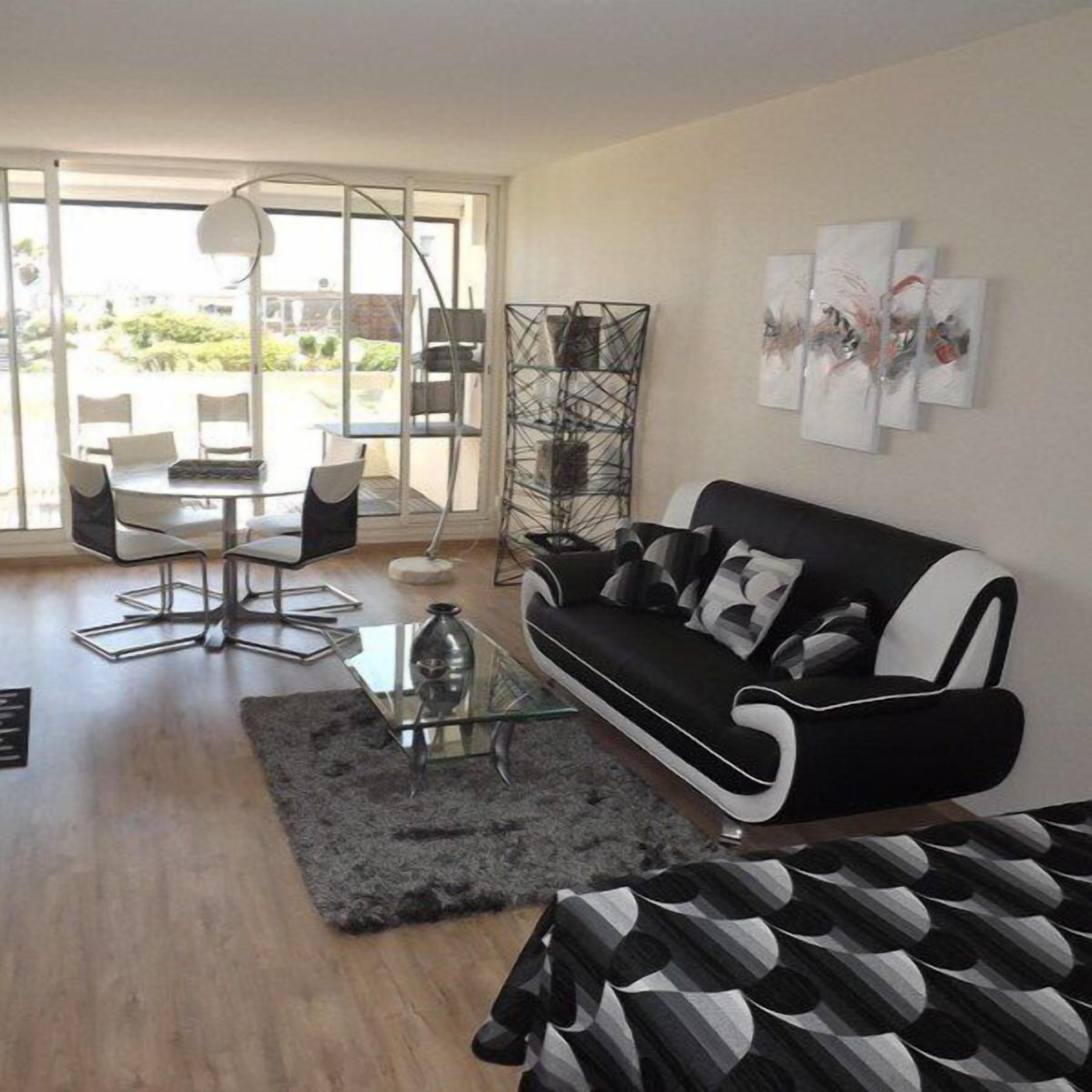 Una sala de estar moderna con un sofá blanco y negro, una mesa de centro de vidrio y un comedor con sillas y una mesa.