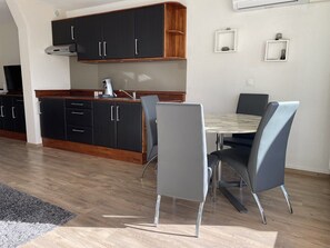 Een moderne keuken met donkere kastjes, een houten aanrechtblad en een ingebouwde kookplaat. Er is een zithoek met een tafel en stoelen.