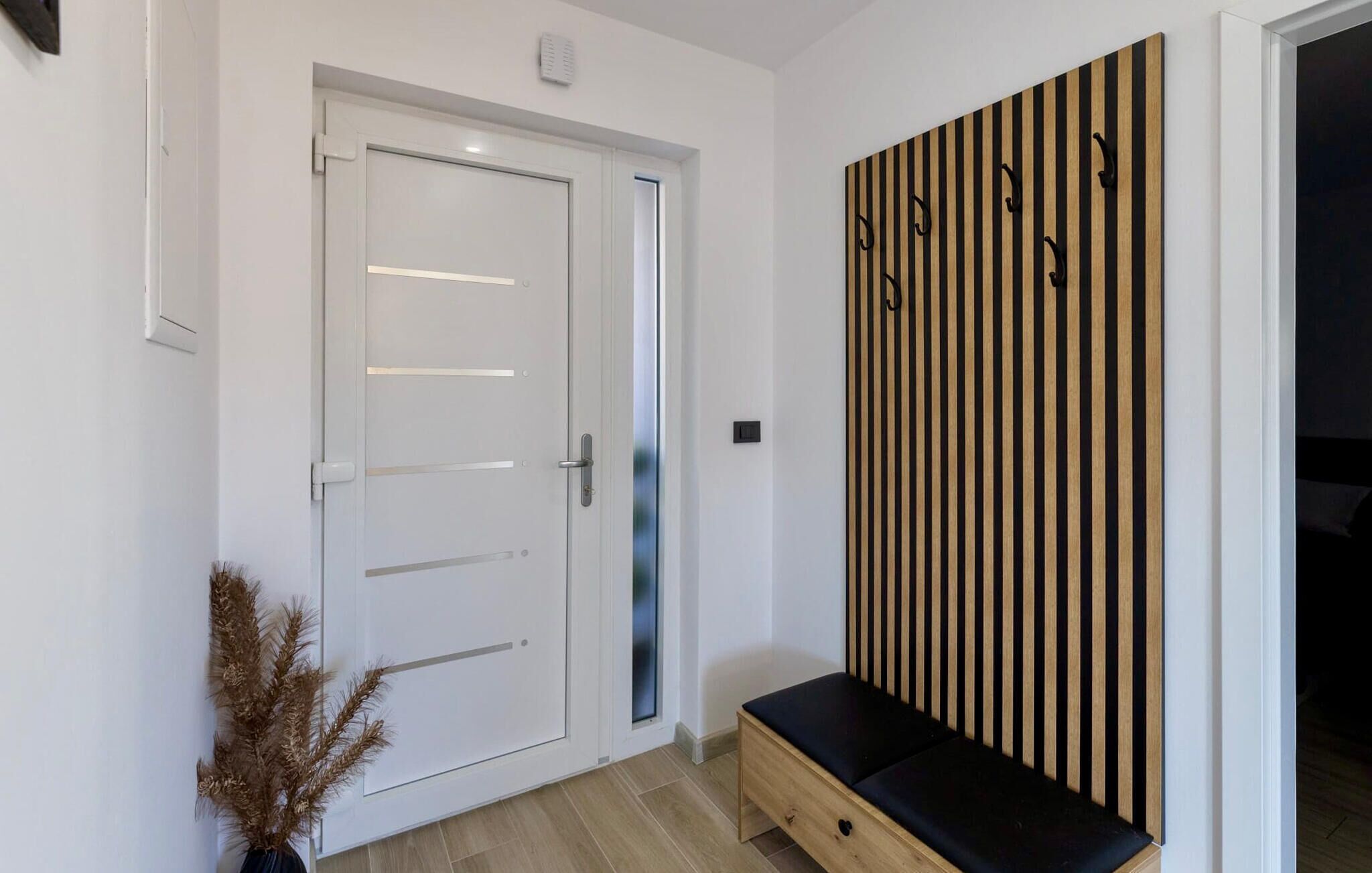 Un pasillo con una puerta blanca, un banco y un perchero de pared.