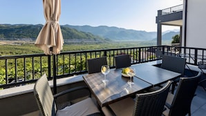 Un balcone con un tavolo apparecchiato per due, con vista su un paesaggio montuoso.