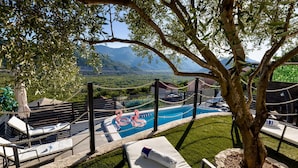 Area piscina con sedie a sdraio, un gonfiabile a forma di fenicottero e una vista panoramica sulle montagne.