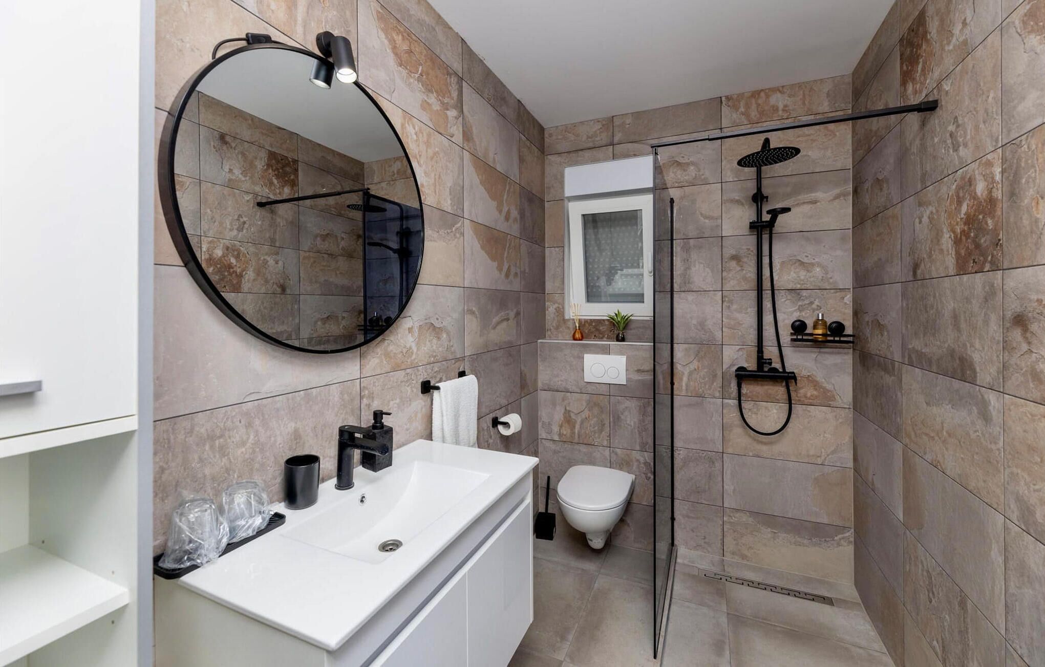 Une salle de bain moderne avec un lavabo blanc, un miroir rond, des toilettes et un espace douche.