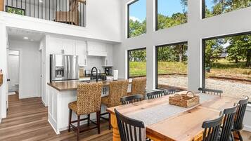 Una cocina moderna con armarios blancos, una mesa de comedor de madera y vistas a un paisaje natural a través de grandes ventanales.